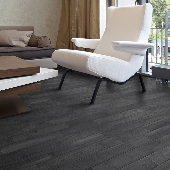 Dettaglio salotto con poltrona bianca e pavimento in gres porcellanato effetto legno rustico della collezione Living di Ceramica Rondine, formato 7.5x45 cm, colore Nero