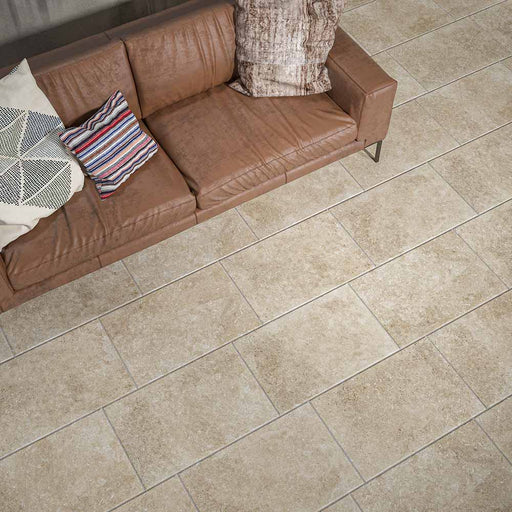 Soggiorno con divano in pelle marrone e pavimento in gres porcellanato effetto pietra leccese. Collezione Dea di Idea Ceramica, Colore Gold Formato 40x60 