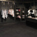 Negozio d'abbigliamento con bancone nero e appendi abiti oro, pavimento in gres porcellanato smaltato opaco effetto pietra naturale ardesia della collezione Ecoslate di Paul & Co Ceramiche, formato 90x90, colore Black