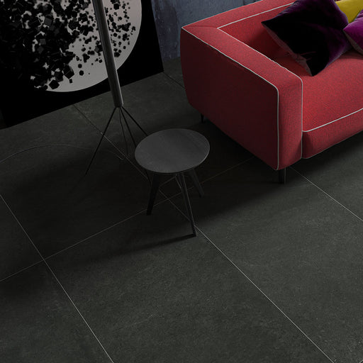 Salotto con divano in tessuto rosso e piastrelle per pavimento in gres porcellanato effetto cemento. Collezione Mistery di Idea Ceramica, Colore Black Formato 60x120 rett 