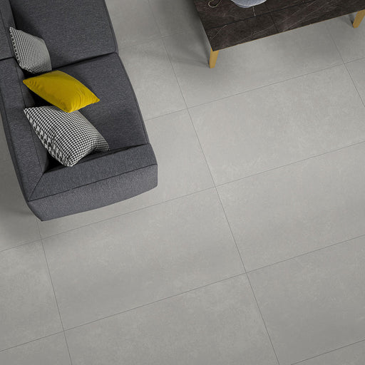 Salotto con divano in tessuto grigio e piastrelle per pavimento in gres porcellanato effetto cemento. Collezione Mistery di Idea Ceramica, Colore White Formato 60x120 rett 