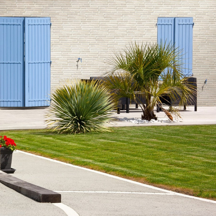 Esterno villa con giardino, infissi azzurri e muro con rivestimento in gres porcellanato effetto mattone in rilievo della collezione Urban nella colorazione Dallas di Keradom