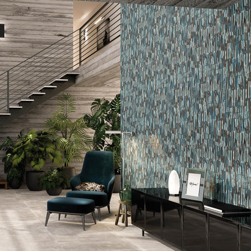 Soggiorno con poltrona e appoggia piedi in tessuto blu scuro, muro con rivestimento in gres porcellanato smaltato opaco effetto cemento DECORATO astratto rigato multicolor della collezione More! di Paul & Co Ceramiche, formato 60x120, colore Bluerain