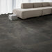 Salotto con divano moderno e pavimento Elea Carbon di Idea Ceramica in gres porcellanato effetto pietra e cemento 90x90