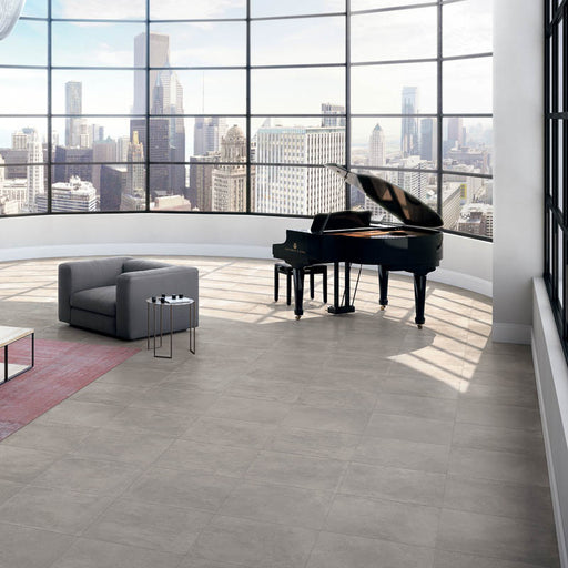 Stanza con poltrona grigia, pianoforte nero lucido e pavimento effetto cemento industriale. Scopri Moov di Ceramiche Keope nel formato 60x60, colore grey.