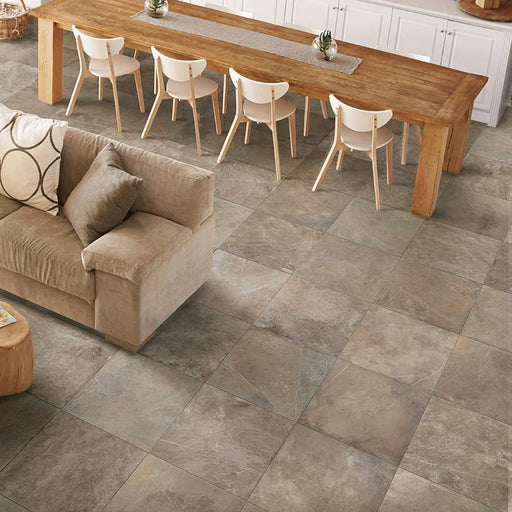 Soggiorno con tavolo grande in legno, divano marrone e pavimento in gres porcellanato effetto pietra naturale della collezione Pietre di Fiume di Ceramica Rondine, formato 60x60 cm, colore Tortora