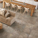 Soggiorno con tavolo grande in legno, divano marrone e pavimento in gres porcellanato effetto pietra naturale della collezione Pietre di Fiume di Ceramica Rondine, formato 60x60 cm, colore Tortora