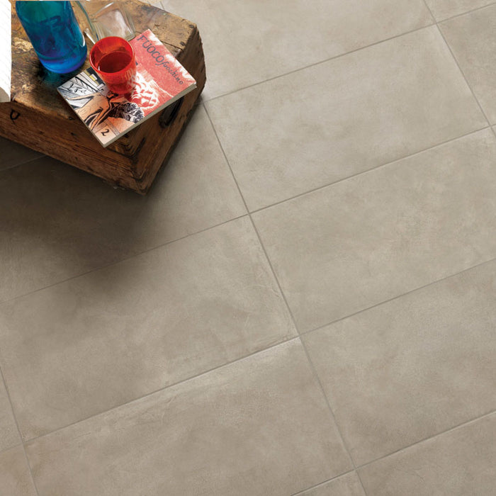 dettaglio con ceppo di legno usato come tavolino appoggiato su pavimento in gres porcellanato smaltato opaco effetto cemento nuvolato dai toni caldi della collezione Baya di Paul & Co Ceramiche, formato 30x60, colore Grey