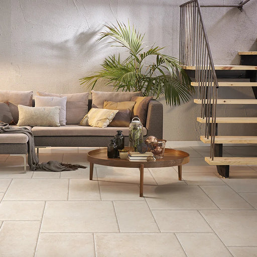 Salotto con divano grigio e scala n legno, pavimento in gres porcellanato effetto pietra leccese della collezione Terre d'Otranto di Ceramica Rondine, formato 60x60 cm con bordo naturale, colore Ivory