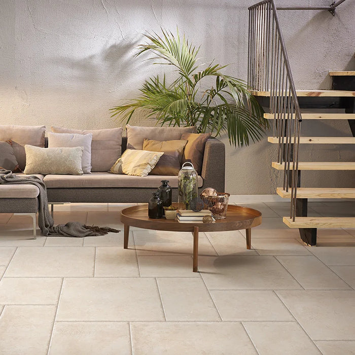 Salotto con divano grigio e scala n legno, pavimento in gres porcellanato effetto pietra leccese della collezione Terre d'Otranto di Ceramica Rondine, formato 60x60 cm con bordo naturale, colore Ivory