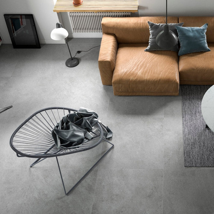 Zona relax con divano in pelle cuoio e sedia in corda. Pavimento in gres porcellanato effetto cemento serie Block di idea Ceramica colore Grey